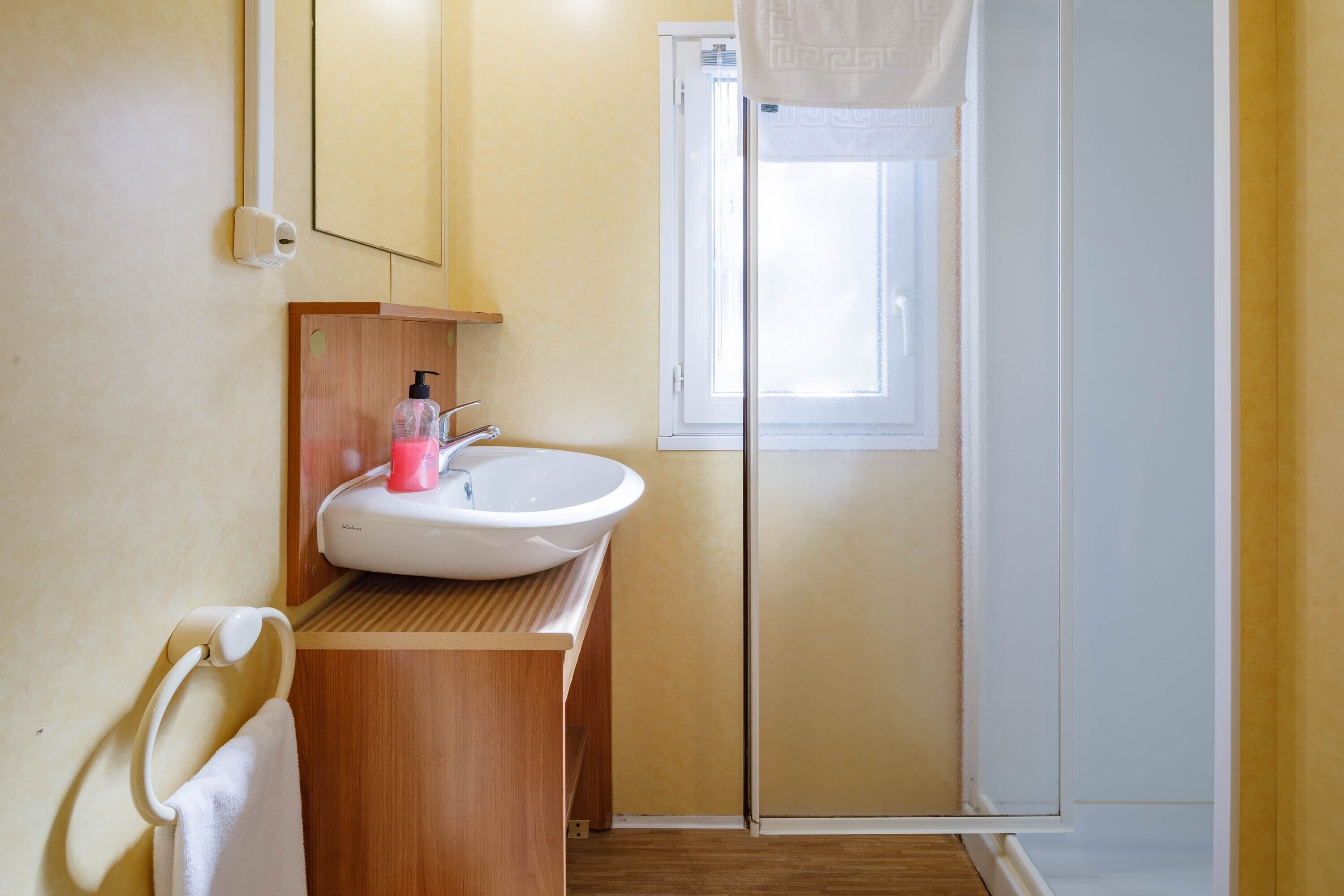 A bathroom with a wooden vanity, a white sink, a towel rack, and a window with a curtain.