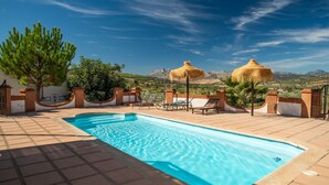 A swimming pool with a clear view of mountains in the background, surrounded by a patio area with chairs and umbrellas.