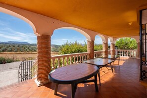 A covered outdoor area with a table and chairs, a white balustrade, and a view of the landscape.