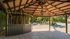 A covered outdoor area with a stone floor, a metal railing, and a thatched roof.