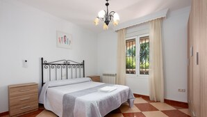 A bedroom with a bed, a nightstand, a dresser, a radiator, a window with curtains, and a chandelier.