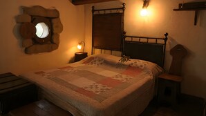 A bedroom with a bed, a round mirror, a wooden headboard, a bedside table, and a wall-mounted light fixture. - Apartment 'Col Di Metino' with Mountain View, Private Garden and Wi-Fi (Gualdo Tadino)