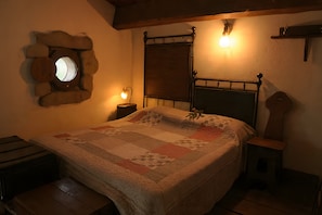 Une chambre à coucher comprenant un lit, un miroir rond, une tête de lit en bois, une table de chevet et un luminaire fixé au mur.