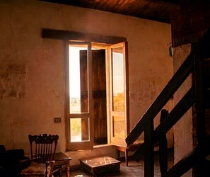 A room with a wooden door leading outside, a small table, a chair, and a staircase.
