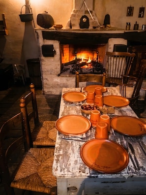 A rustic dining area with a fireplace, wooden chairs, and a table set with orange plates and cups.
