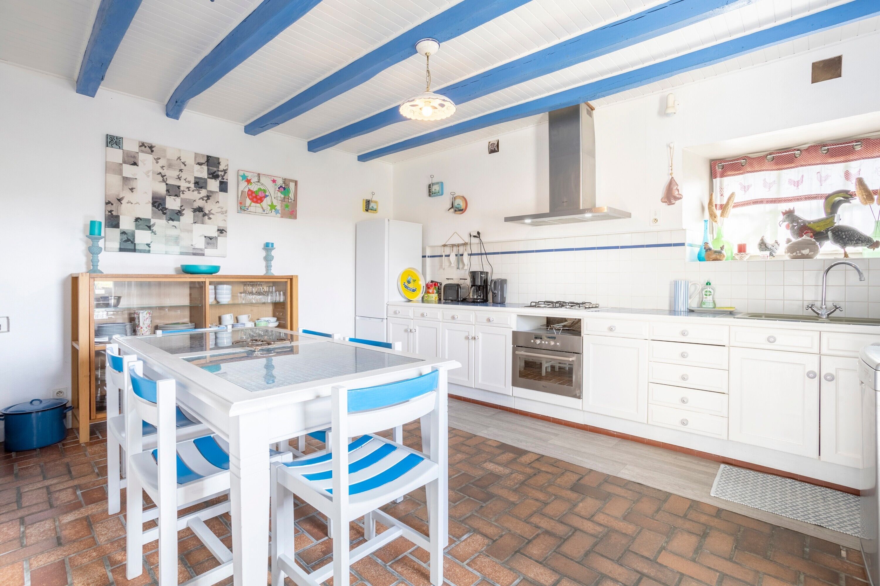 Una cocina con armarios blancos, techo azul y una zona de comedor con sillas blancas.