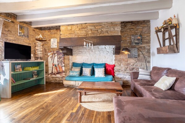 A cozy living room with a stone wall, a wooden sofa, a brown leather couch, a wooden coffee table, and a television on a stand.