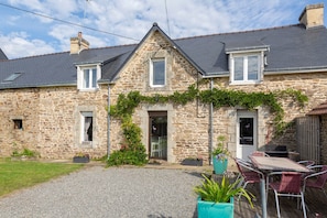 Une maison en pierre avec une allée en gravier, une terrasse avec des chaises et un petit jardin.