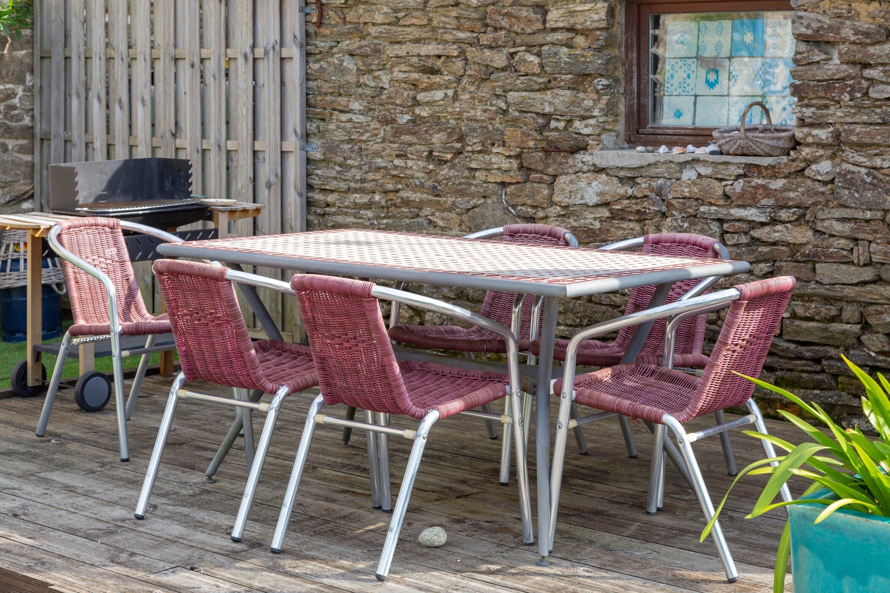 Un patio con una mesa, sillas, una parrilla y un muro de piedra.