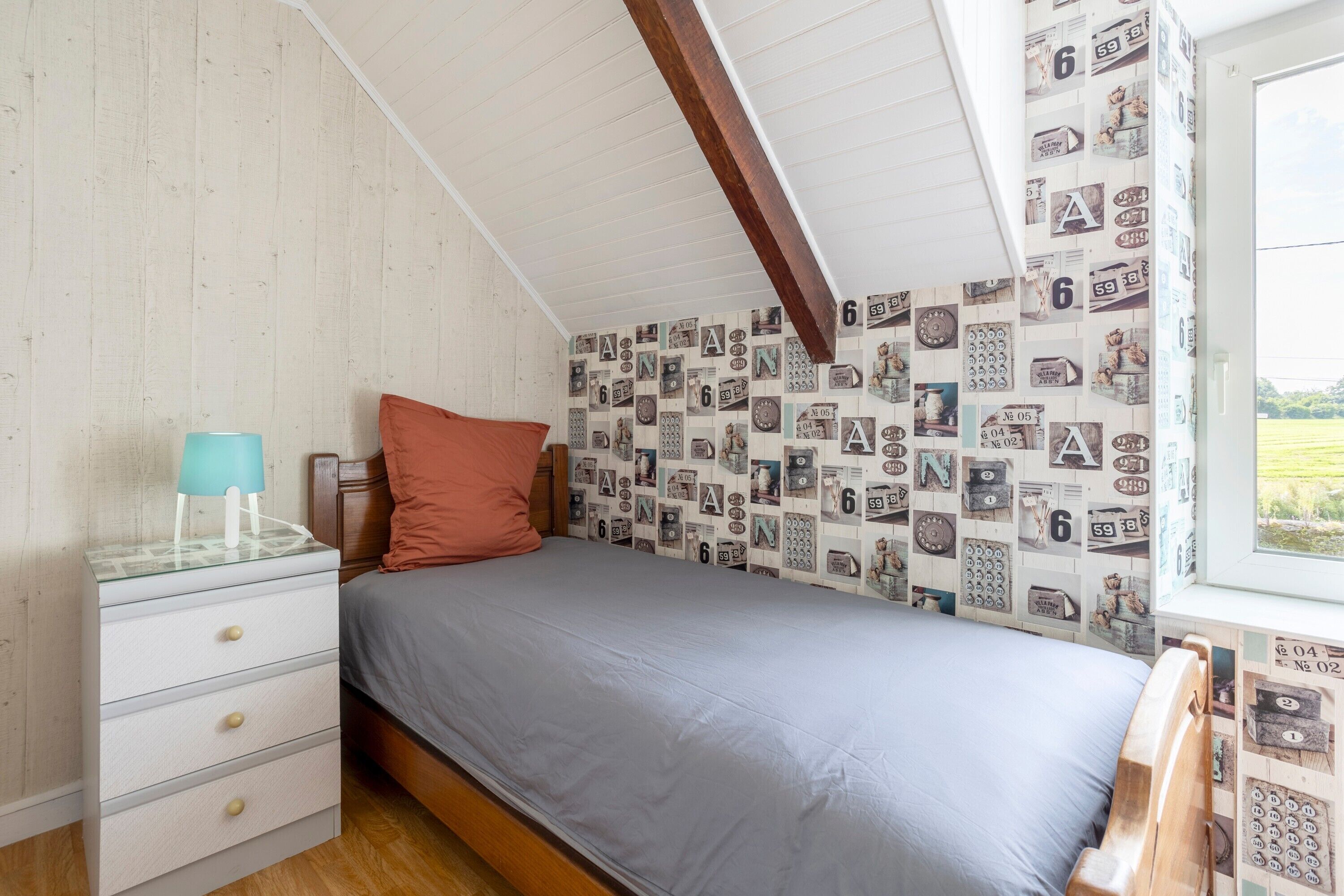 Un dormitorio con cama, mesita de noche, lámpara y una pared con números de teléfono antiguos.