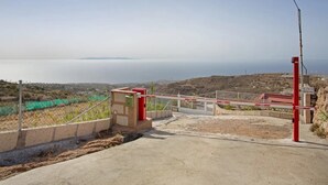 Ein verschlossenes Tor mit Metallgitter, ein Betonweg und Blick auf eine Küstenlandschaft.