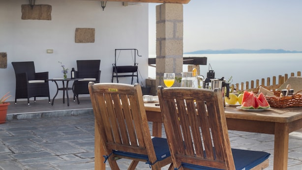 Un patio con sillas y una mesa de madera dispuestas para el desayuno, con vistas a un cuerpo de agua.