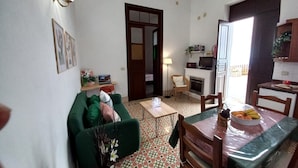 Una sala de estar con un sofá verde, una mesa de comedor con sillas, una chimenea y una zona de cocina con armarios y un televisor.