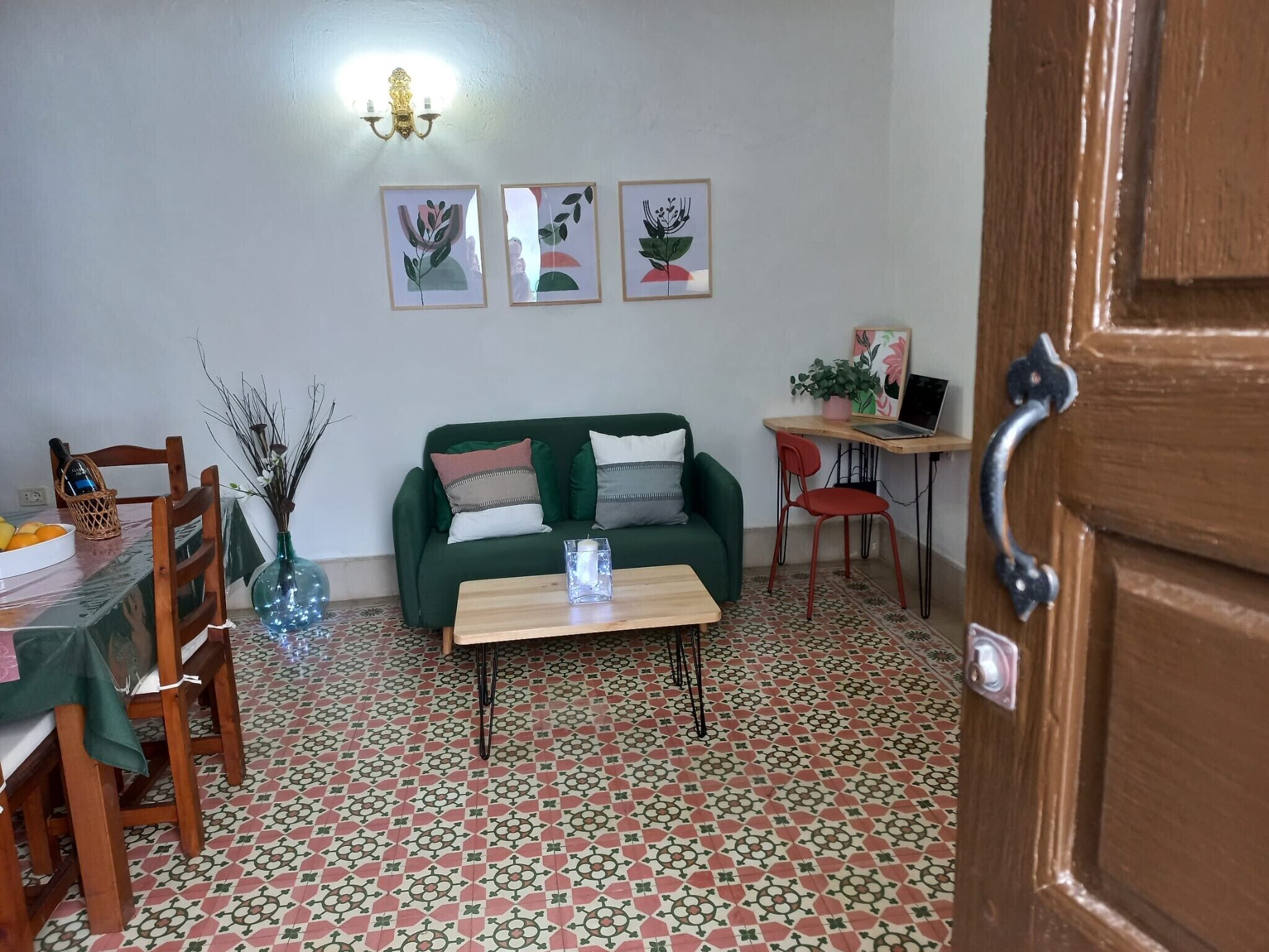 A living room with a green sofa, a wooden coffee table, a dining table with chairs, and a patterned floor.