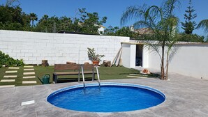 Una piscina con un muro de ladrillo blanco, un banco de madera y un árbol pequeño.