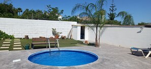En swimmingpool med en hvid murstensvæg, en træbænk og et lille træ.