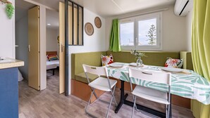 Un espacio habitable compacto con kitchenette, un comedor con mesa y sillas, un sofá y una ventana con vistas a un árbol.