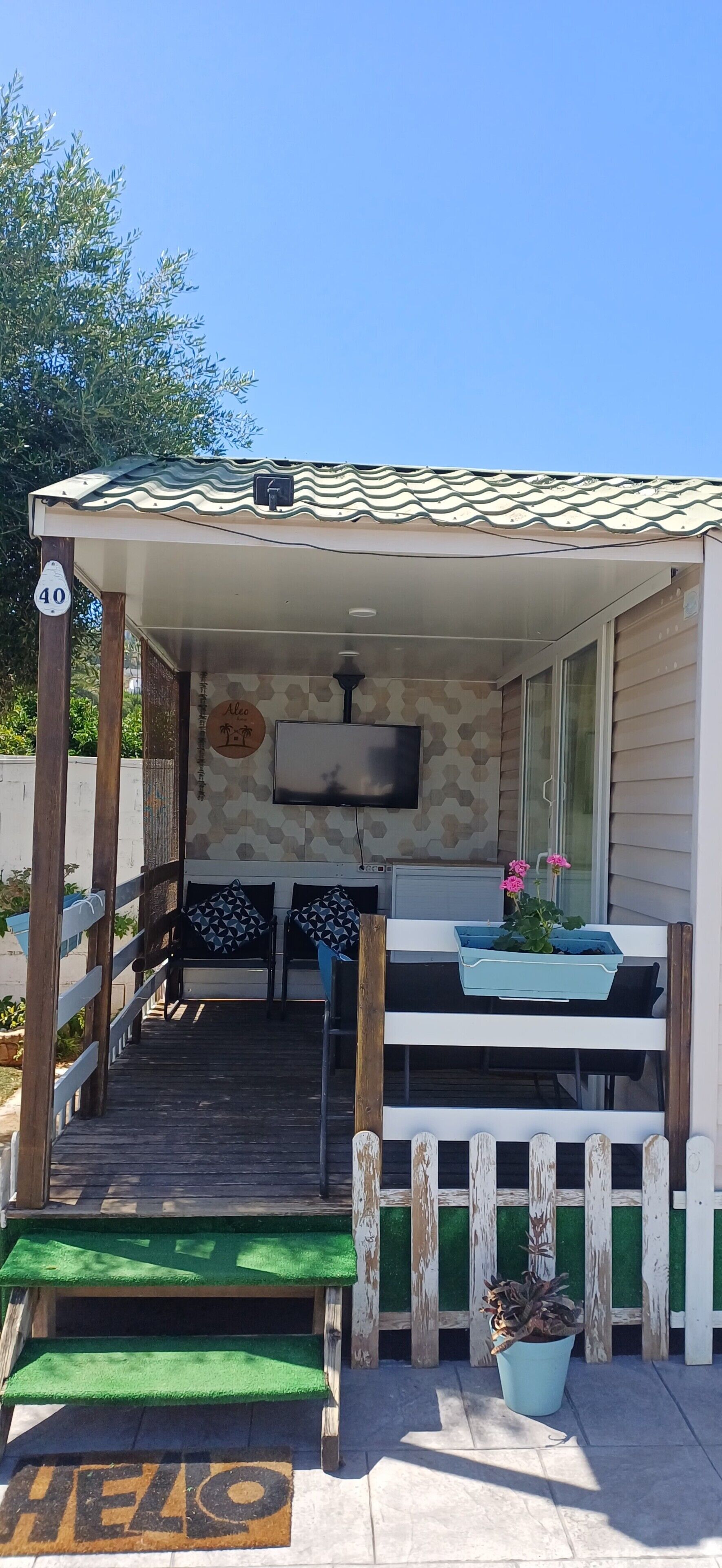 A small, single-story structure with a porch, a television mounted on the wall, and a small seating area with a table and chairs.