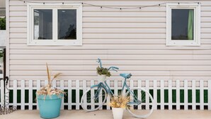 Una casa con cerca de piquetes blancos, una bicicleta azul con cesto y una planta en maceta.
