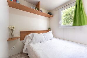 Ett sovrum med en säng, ett fönster med en grön gardin och trähyllor med böcker och dekorativa föremål.