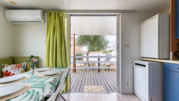 Una habitación con cama, una mesa de comedor con platos, un refrigerador pequeño y una ventana con cortinas.
