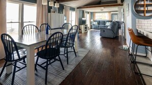 Amplia sala de estar con mesa y sillas de comedor, un sofá y una zona de cocina con un armario blanco.