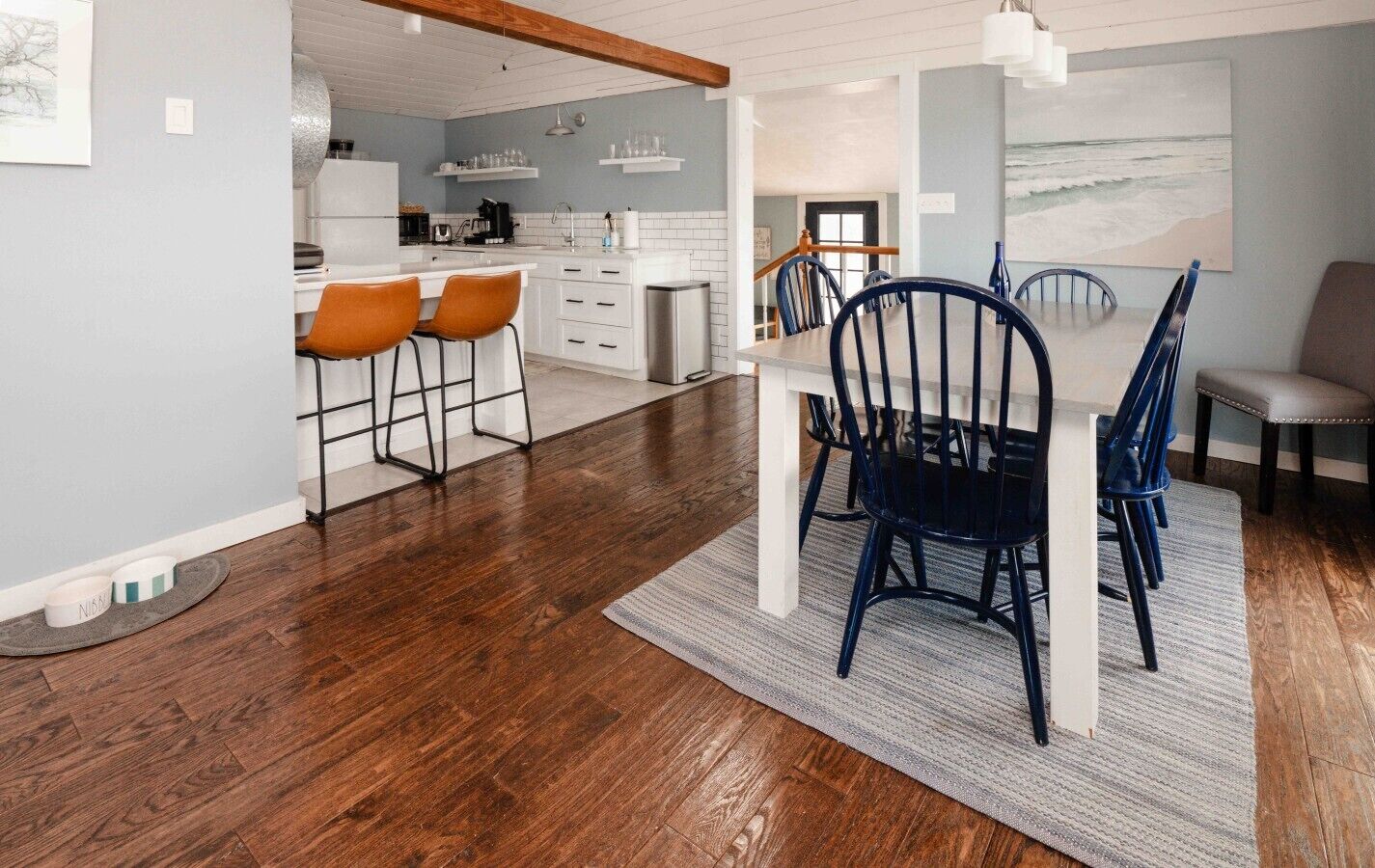 Une cuisine moderne avec des meubles blancs, un coin repas comprenant une table blanche et des chaises bleues, et un plancher en bois.