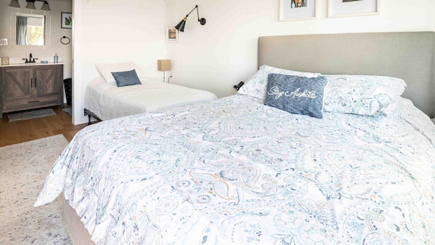 Ein Schlafzimmer mit einem großen Bett, einem Einzelbett, einem Schminktisch, einem Spiegel und einer Wandlampe.