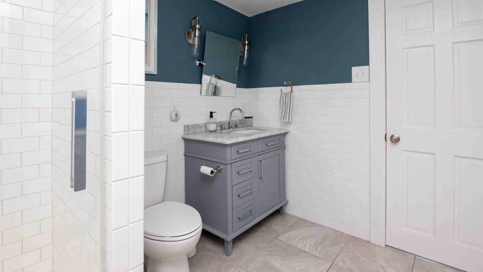 Une salle de bain avec des toilettes blanches, un meuble-lavabo gris, un miroir et une douche.