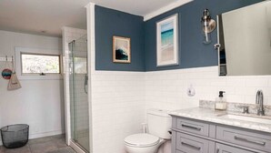 Un baño con cabina de ducha de vidrio, inodoro y tocador con lavamanos.