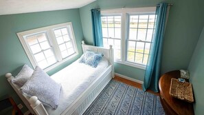 A single-bed room with a window, a bedside table, and a rug.