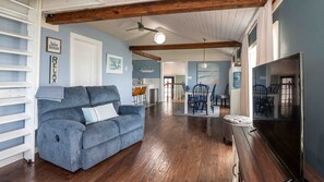 A living room with a blue sofa, wooden flooring, a ceiling fan, and a TV.