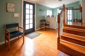 A room with a wooden floor, a bench, a chair, a staircase, and a door with a window.