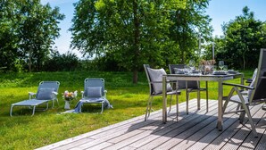 Ein Essbereich im Freien mit Holzdeck, Metallstühlen und einem Tisch, der für eine Mahlzeit gedeckt ist.