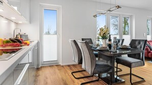 Eine moderne Küche mit Essbereich, Holzboden, weißen Schränken und einem großen Fenster.