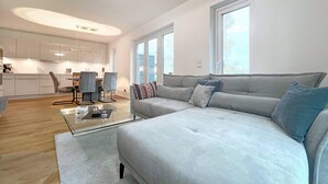 Ein modernes Wohnzimmer mit einem grauen Sofa, einem Glastisch und einem Essbereich mit Stühlen und einem Tisch.