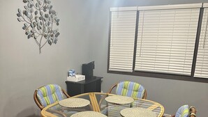 Un coin repas avec une table à plateau en verre, entourée de chaises en osier dotées de coussins à rayures.
