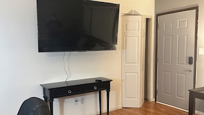 Un salon avec un téléviseur à écran plat fixé au mur, un fauteuil en cuir noir, un plancher en bois et une porte fermée.