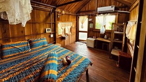 A wooden cabin with a large bed, a kitchenette, and a window with curtains.