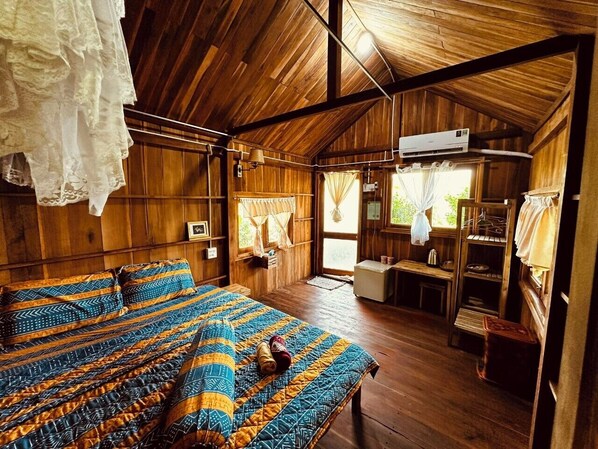 A wooden cabin with a large bed, a kitchenette, and a window with curtains.