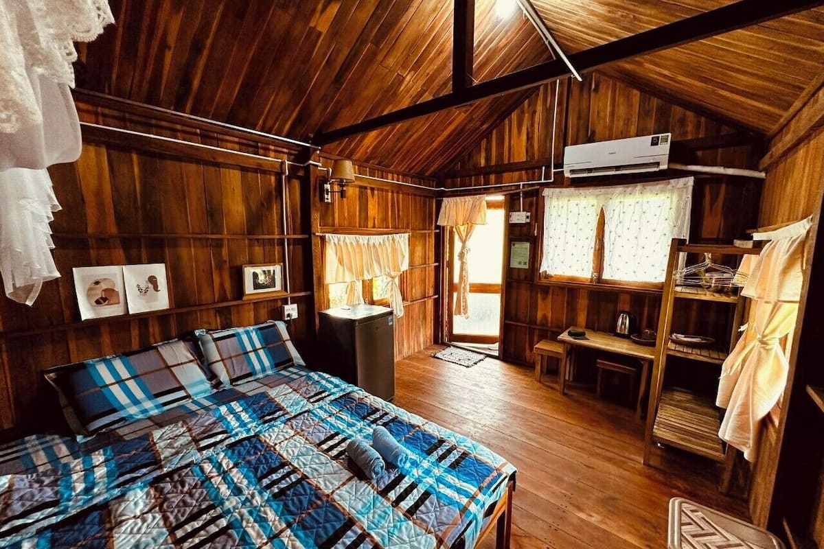 Une cabane en bois rustique comprenant un grand lit, une petite kitchenette et un coin repas.