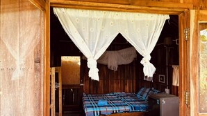 A wooden room with a bed, a small cabinet, and a mosquito net.
