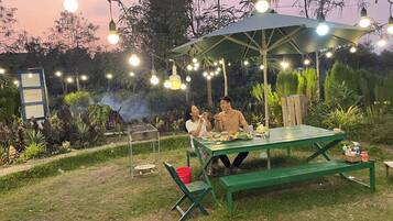 A picnic setup with a green table and benches, surrounded by string lights and greenery.