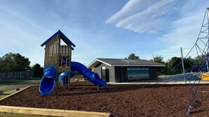Une aire de jeux avec un toboggan et des structures d’escalade, un bâtiment portant l’inscription « PARC DE LA STATION BALNÉAIRE DE PODGORIA », et une zone d’escalade protégée par des filets.