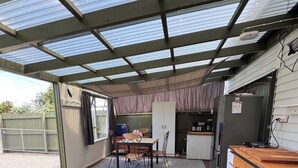 Un espace extérieur abrité doté d’une terrasse en bois, d’une table avec des chaises, d’un réfrigérateur et d’un plan de travail de cuisine.
