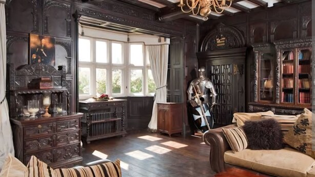 A room with a high ceiling, exposed beams, a chandelier, a large window, a statue, a wooden cabinet, and a sofa. - Caverswall Castle - Grade 1 Listed Historic Castle - Inquire for best quote now (Caverswall)