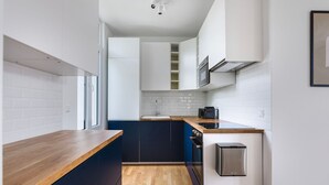 A modern kitchen with white cabinets, a wooden countertop, and a stainless steel refrigerator.