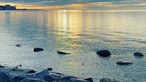A coastal scene with a calm sea, rocky shoreline, and a cloudy sky reflecting on the water.