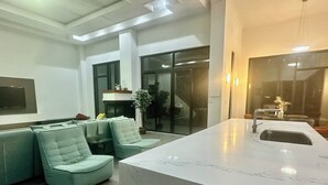 A modern living room with a marble island, green cushioned seating, a flat-screen TV, and a large window.