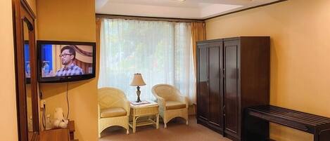 Una habitación de hotel con televisión, dos sillas, una mesita con lámpara, armario y cama.